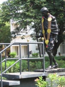 Une statue de Gandhi qui marche vers une passerelle, dans un jardin